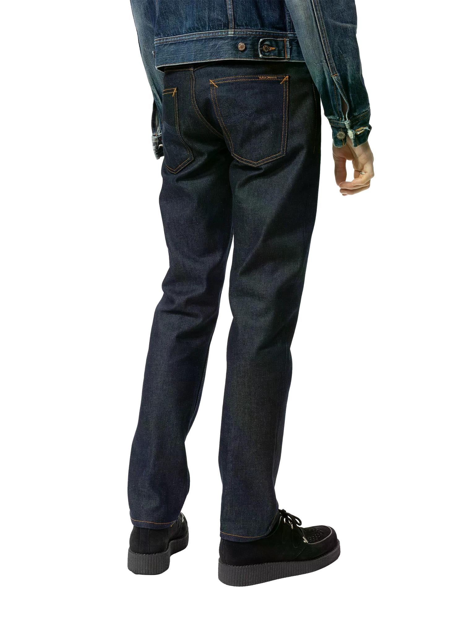 Mørkeblå Nudie Jeans Ollie Dry Abyss jeans av bomull med klassisk snitt og synlige sømmer, vist på en flat overflate.