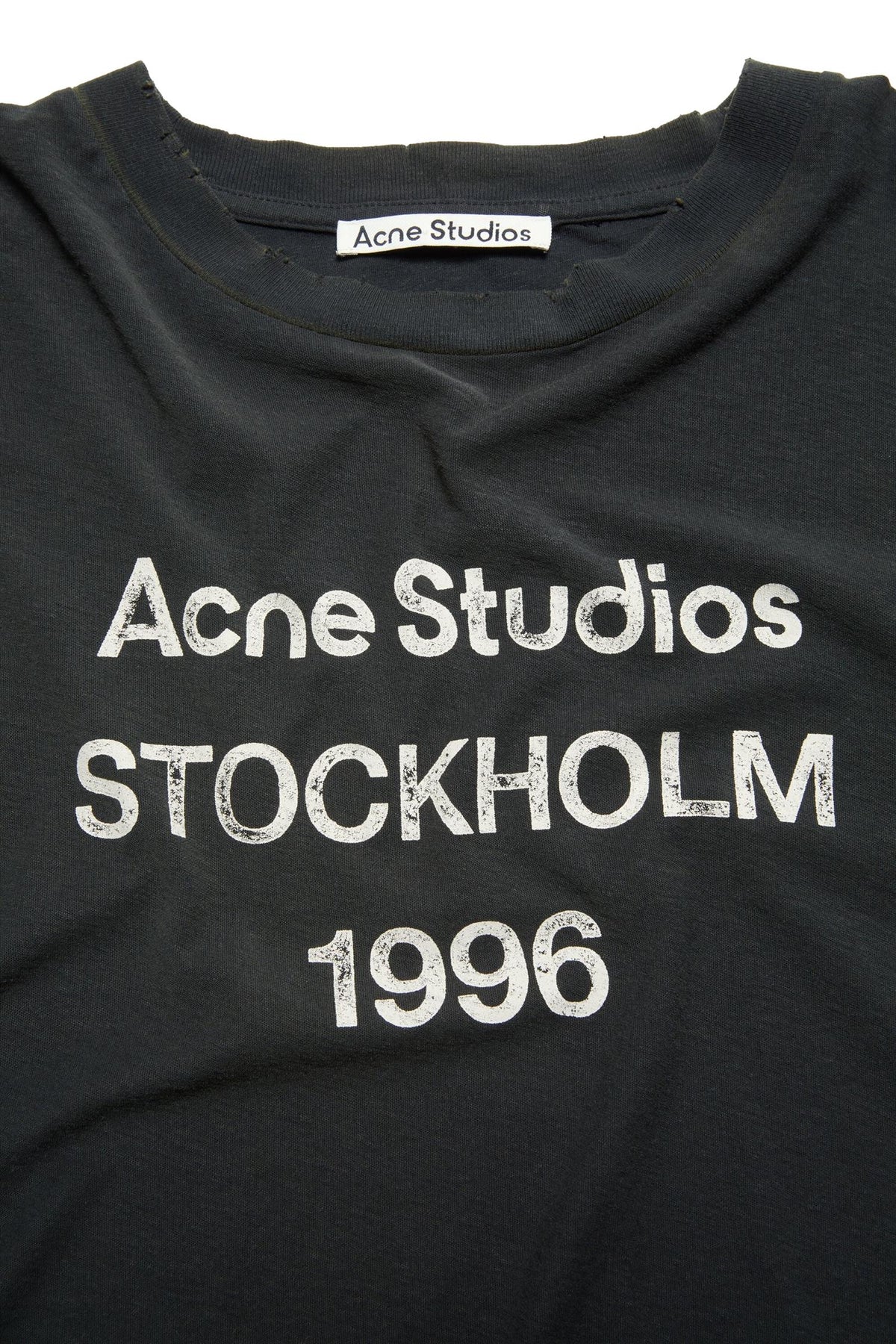 Sort Acne T-skjorte med logo og vasket design, laget av mykt stoff, vises i bilde.