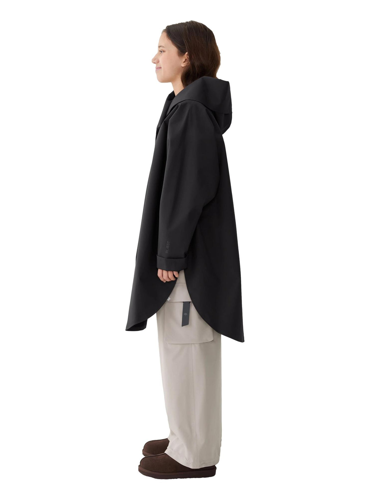 Blæst Bergen Mini Poncho Black jakke i sort stoff, vist på modell foran utendørsbakgrunn.
