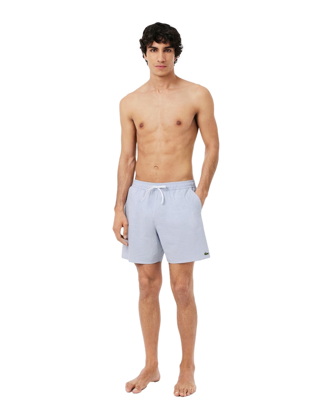 Lacoste badebukser med midilengde, hvite og blå striper, teksturert stoff, egnet for svømming og strandbruk.