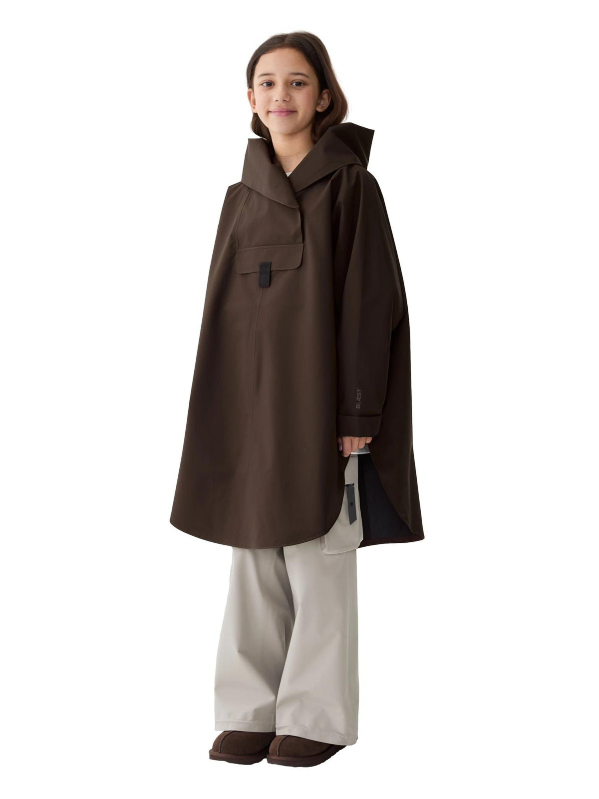 Blæst Bergen Mini Poncho Java jakke i brun med hette, vist på modell foran en utendørs bakgrunn