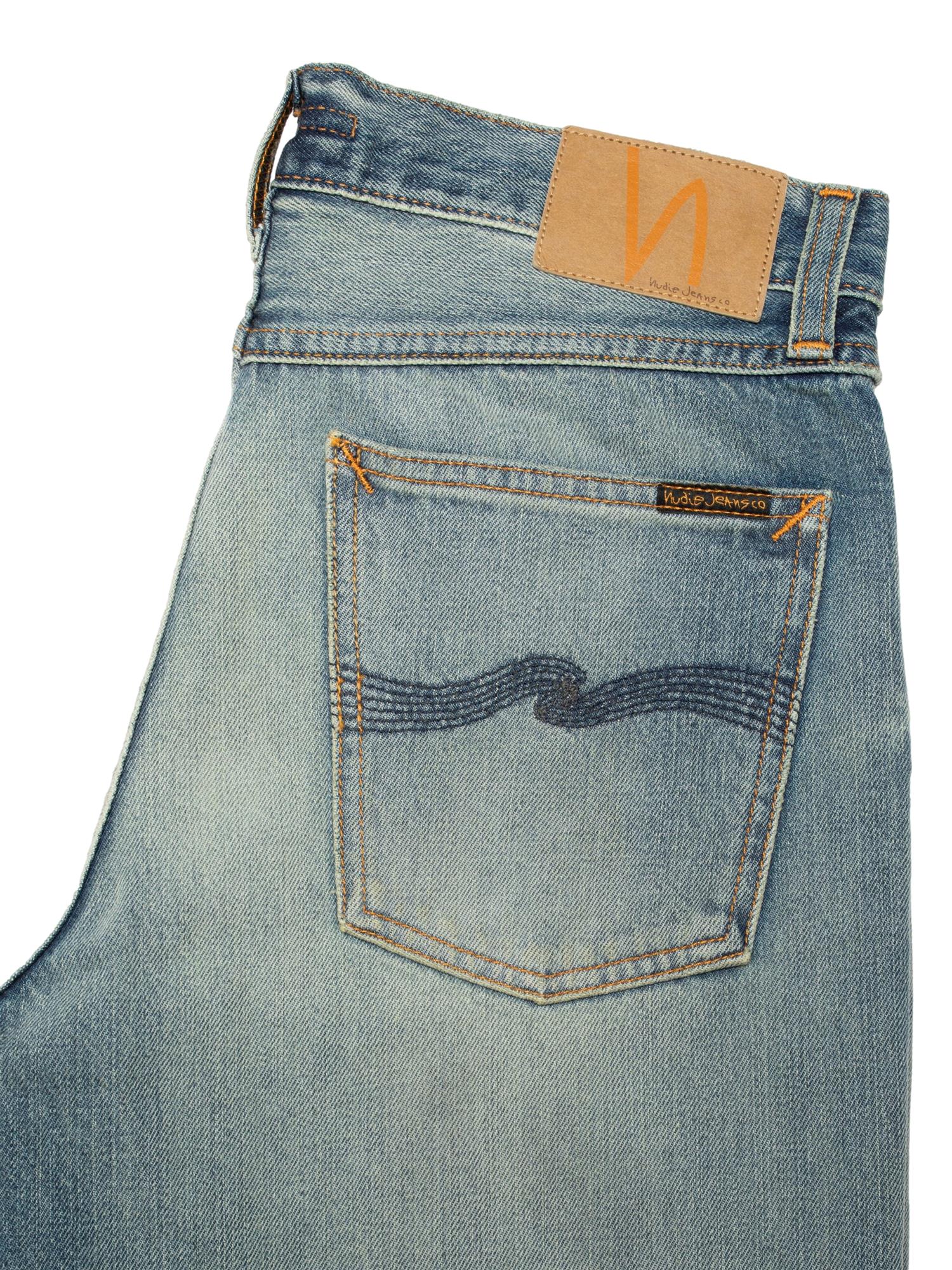 Nudie Jeans Rad Rufus jeans i beige og blå med slitt vask, vises på modell i et naturlig miljø.