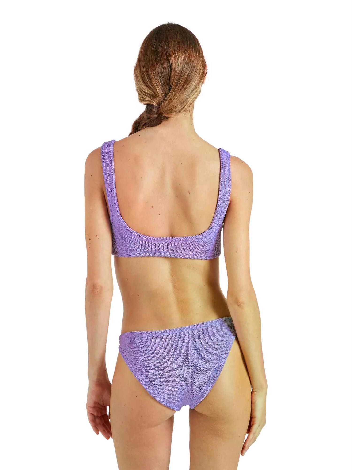 Hunza G Xandra bikini i lilla, tettsittende badetøy med glatt elastisk stoff, vist på modell foran en nøytral bakgrunn.