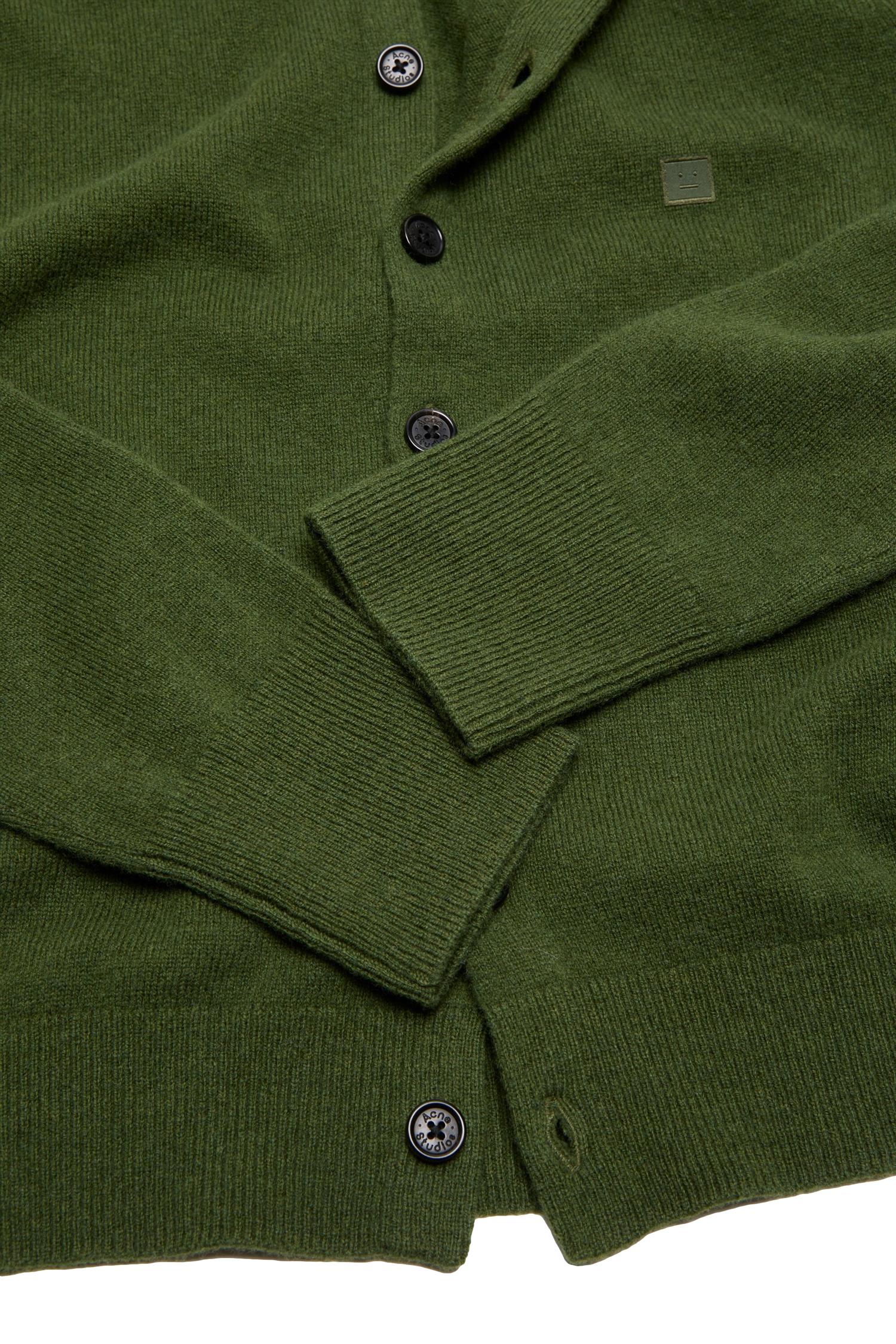 Grønn Acne fitted cardigan i myk ull med knappelukking, vist på modell foran lys bakgrunn.