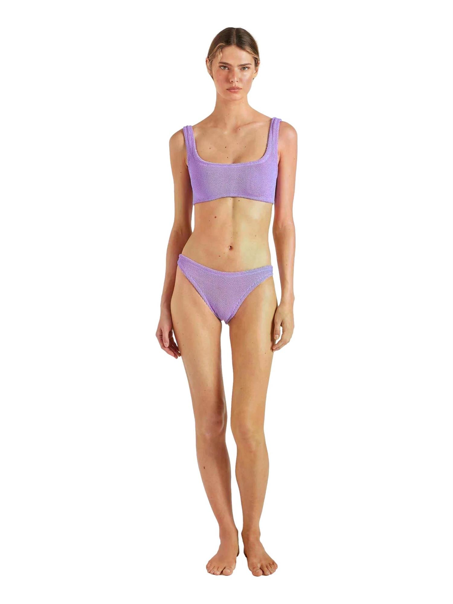 Hunza G Xandra bikini i lilla, tettsittende og strikket i elastisk materiale, utendørs med sollys i bakgrunnen.