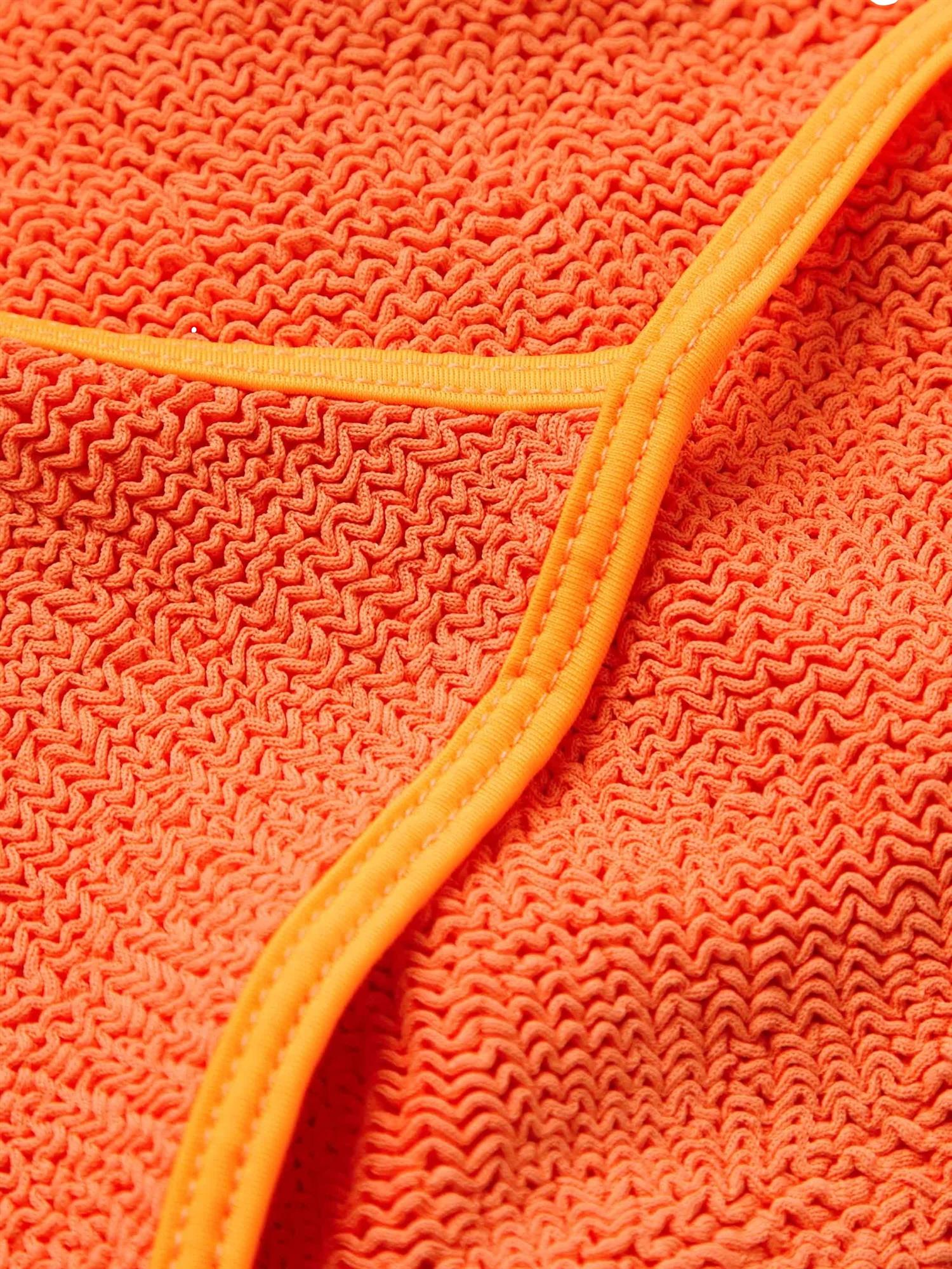 Oransje badedrakt fra Hunza G Pamela Swim med glatt stoff og v-hals, vist på modell i vannet.